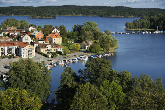 Liten stad vid vattnet syns från ovan med skog i förgrunden.