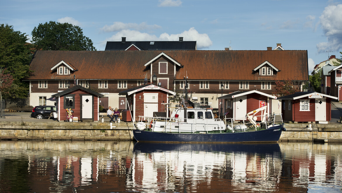 Ett rött större hus och mindre röda stugor intill vattnet där en båt ligger.
