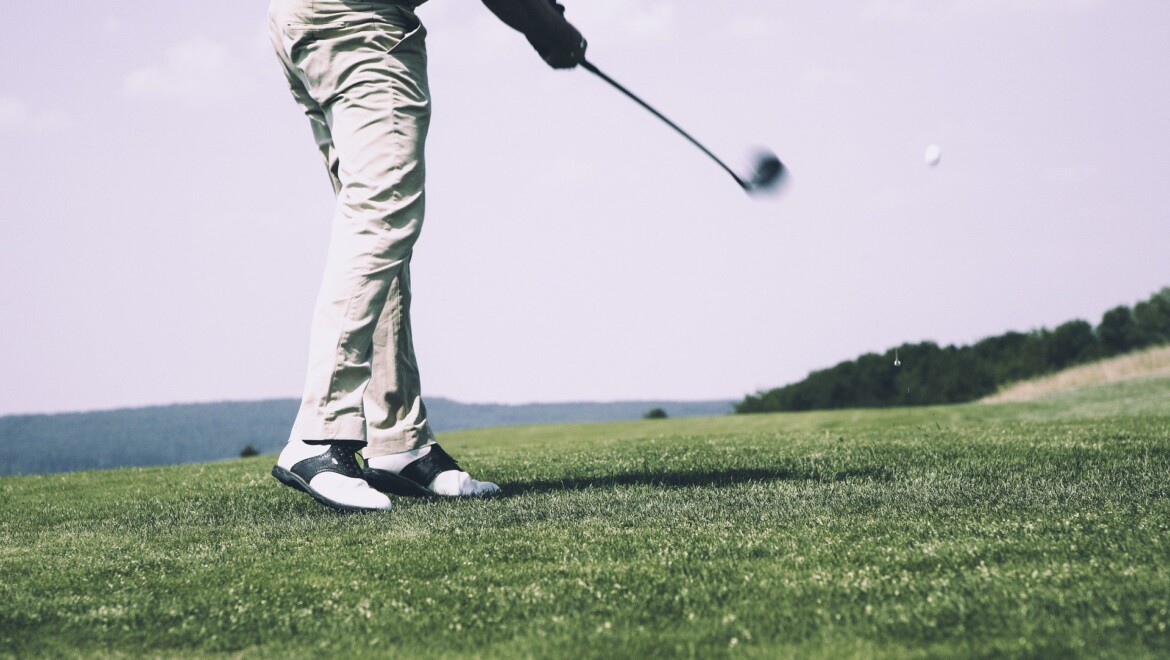 En person spelar golf i vita kläder.