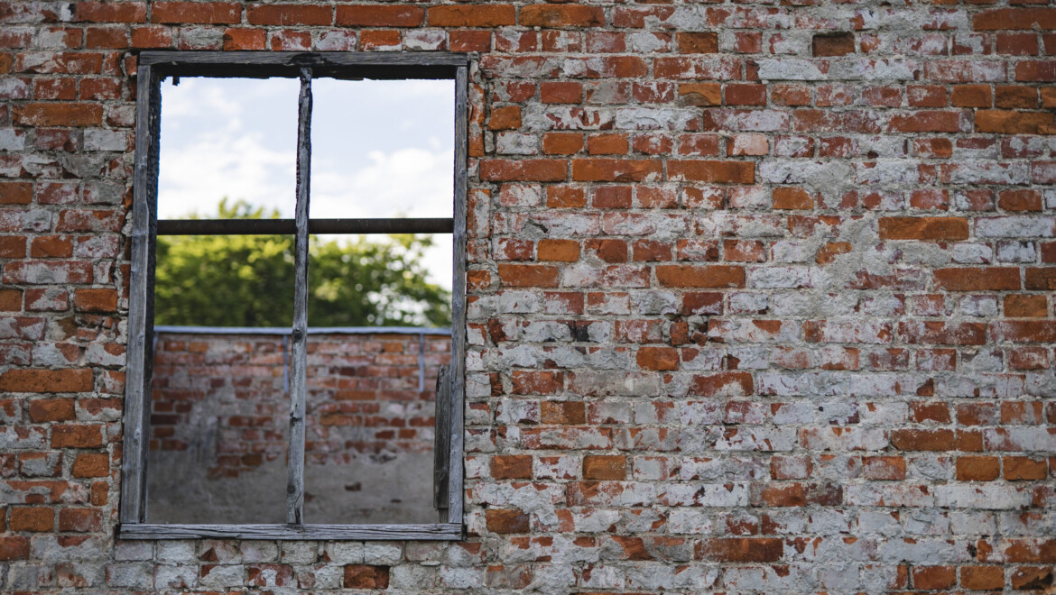 Närbild på gammalt tegel med en fönsterbåge till vänster i bild.