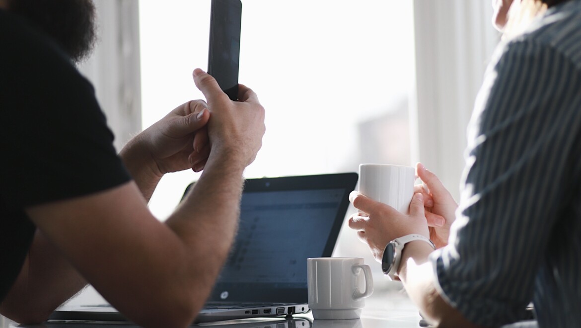 Två personer sitter vid ett bord och har en laptop och kaffekoppar framför sig.