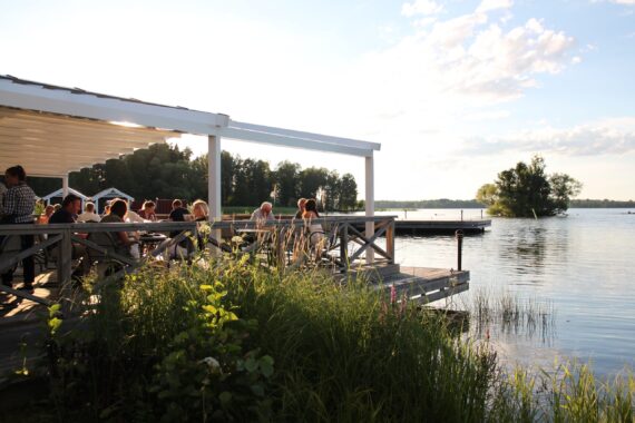Solnedgång över en sjö. Till vänster skymtar en terrass med människor sittandes vid bord.