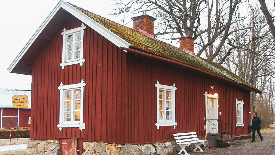 Ett rött hus omgiven med vita knutar och en vit bänk framför entrén. Taket är klätt av mossa.