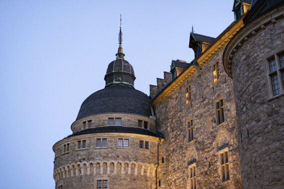 Ett svagt upplyst torn av Örebro slott mot blå himmel i kvällsljus.