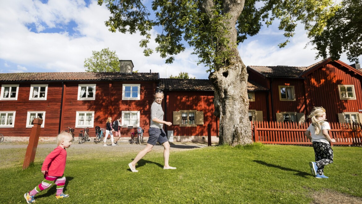 Två små barn och en kvinna springer på gräset i Wadköping.