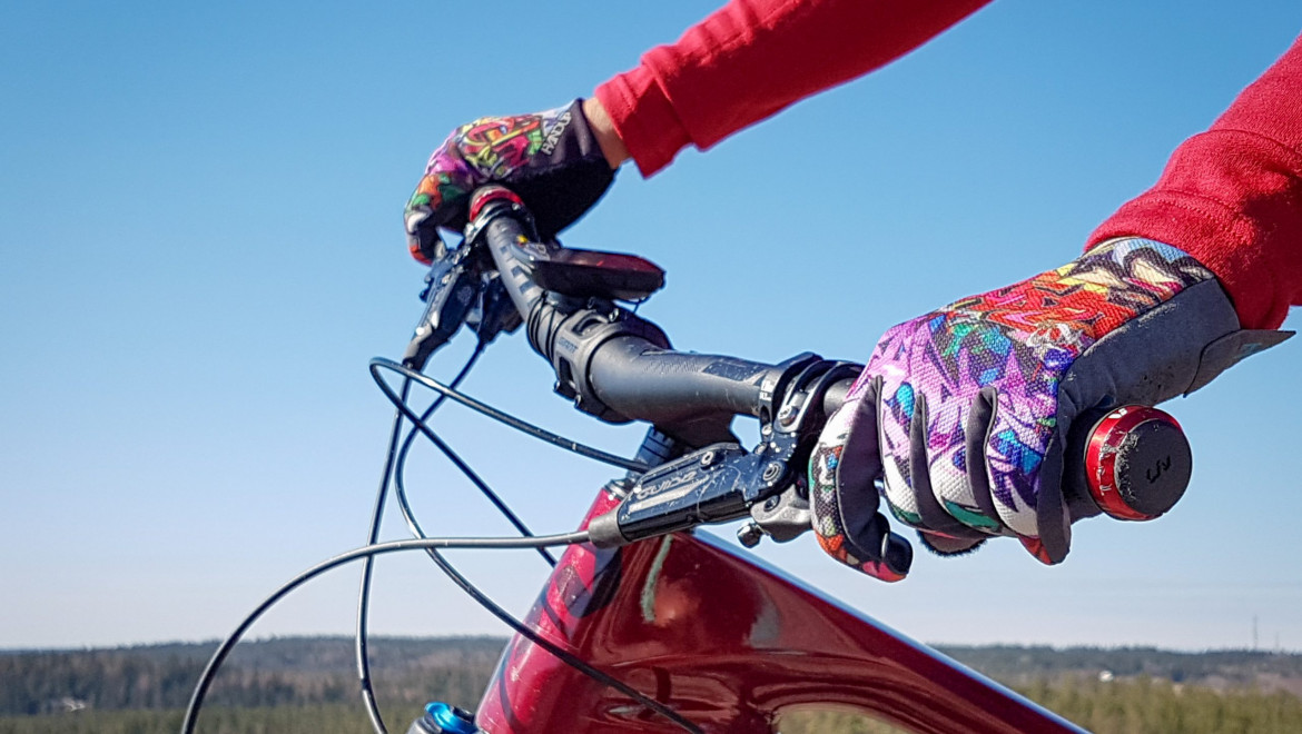 Två mönstrande handskbeklädda händer håller om ett rött cykelstyre.
