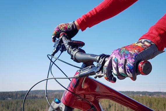 Två mönstrande handskbeklädda händer håller om ett rött cykelstyre.