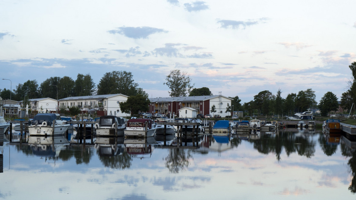 Många båtar ligger förtöjda i en småbåtshamn. Himlen är gråblå och speglar sig i vattnet.