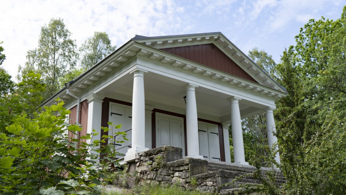 Ett rött och vitt hus med piedestaler står på en upphöjning av stenar.