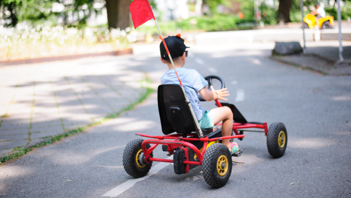 En liten pojke som kör som sitter i en röd/svart trampbil.