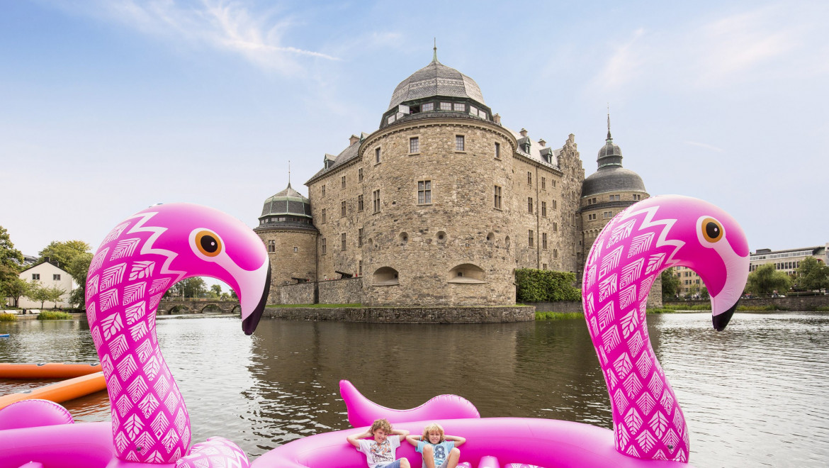 Två uppblåsbara flamingos i vattnet framför Örebro slott.