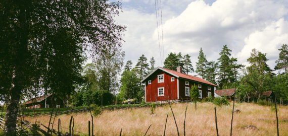 Ett rött hus omgiven av ängar på svensk landsbygd.