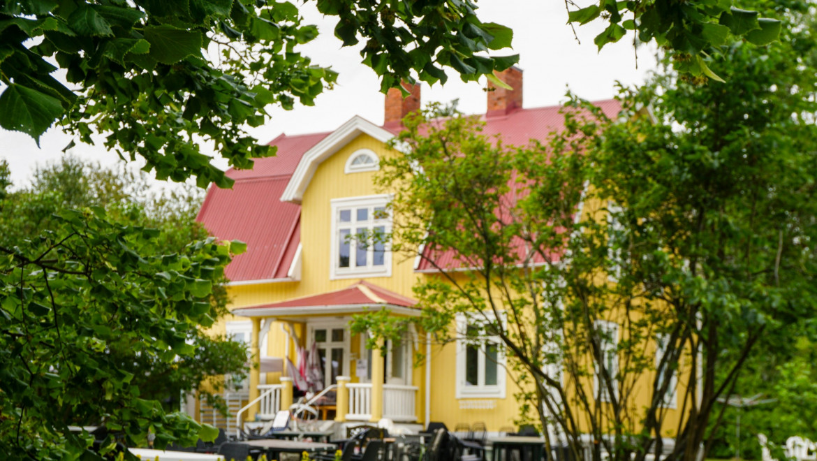 Ett gult trähus med bord och stolar framför entrén.