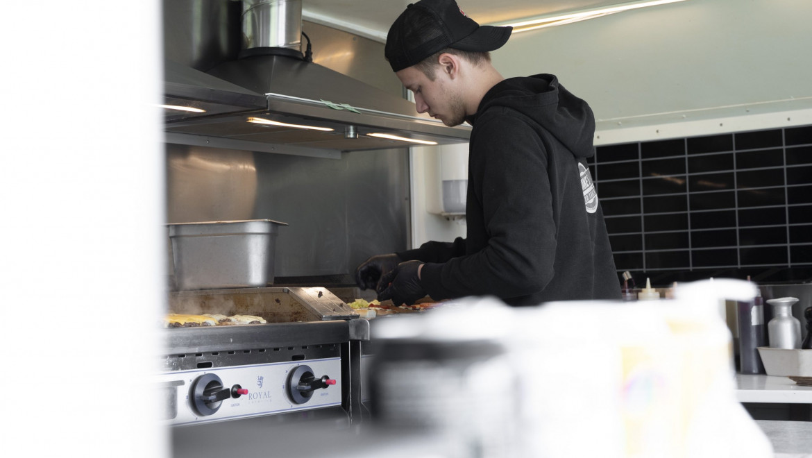 en ung man med keps bakochfram steker hamburgare i Mikes foodtruck.