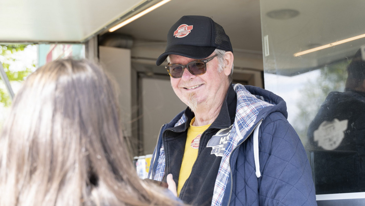 Mike från Mikes foodtruck, iklädd keps och solglasögon, ler mot en mörkhårig kvinna som syns bakifrån