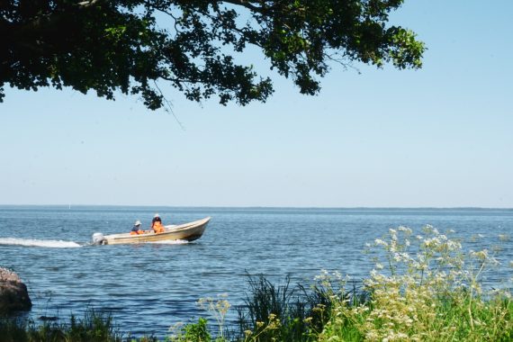 Två fiskare med orange byxor åker i en liten eka på sjön.