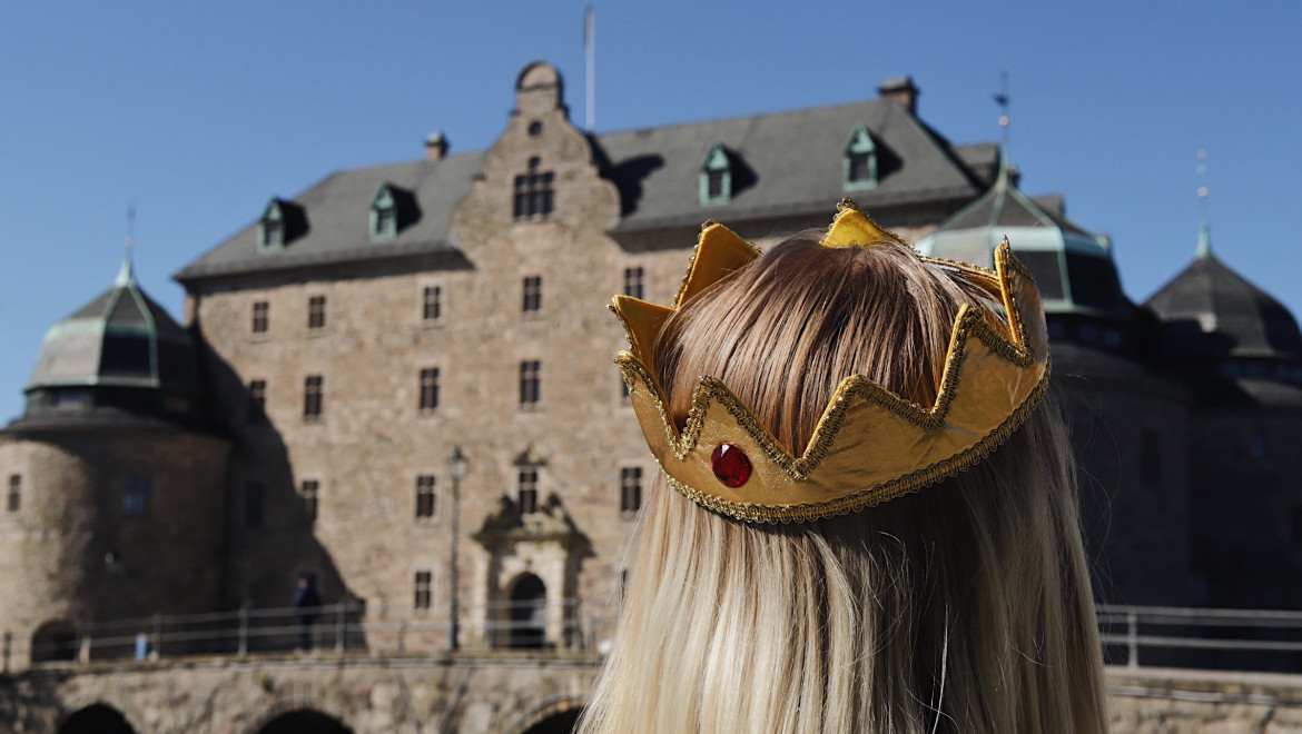 En tjej med krona i tyg står framför Örebro slott.