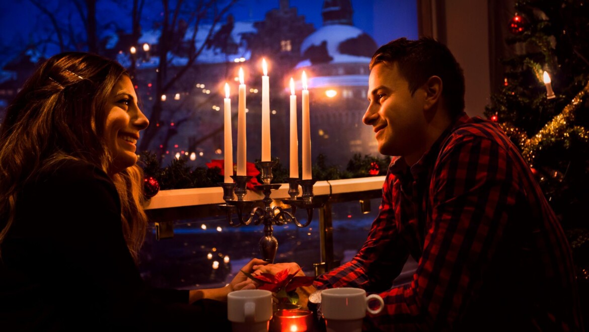 Två personer på restaurang håller varandra i handen och har tända ljus vid bordet.