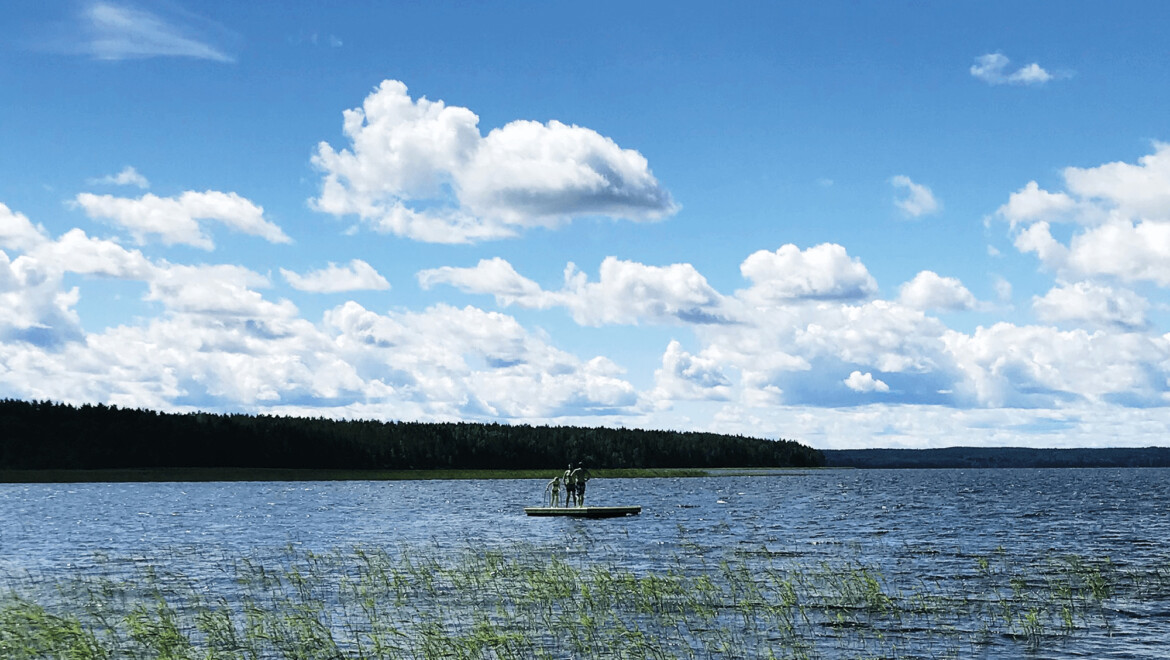 En badbrygga med tre personer i en sjö.