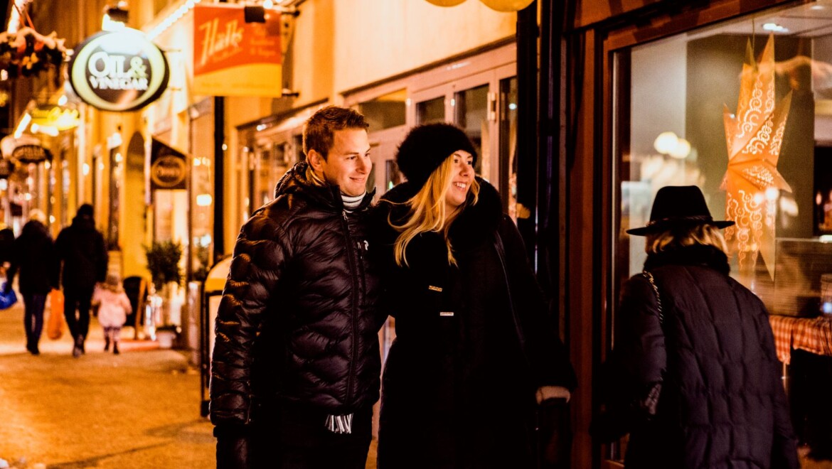 Två personer står tätt intill varandra och tittar in genom en juldekorerat skyltfönster.