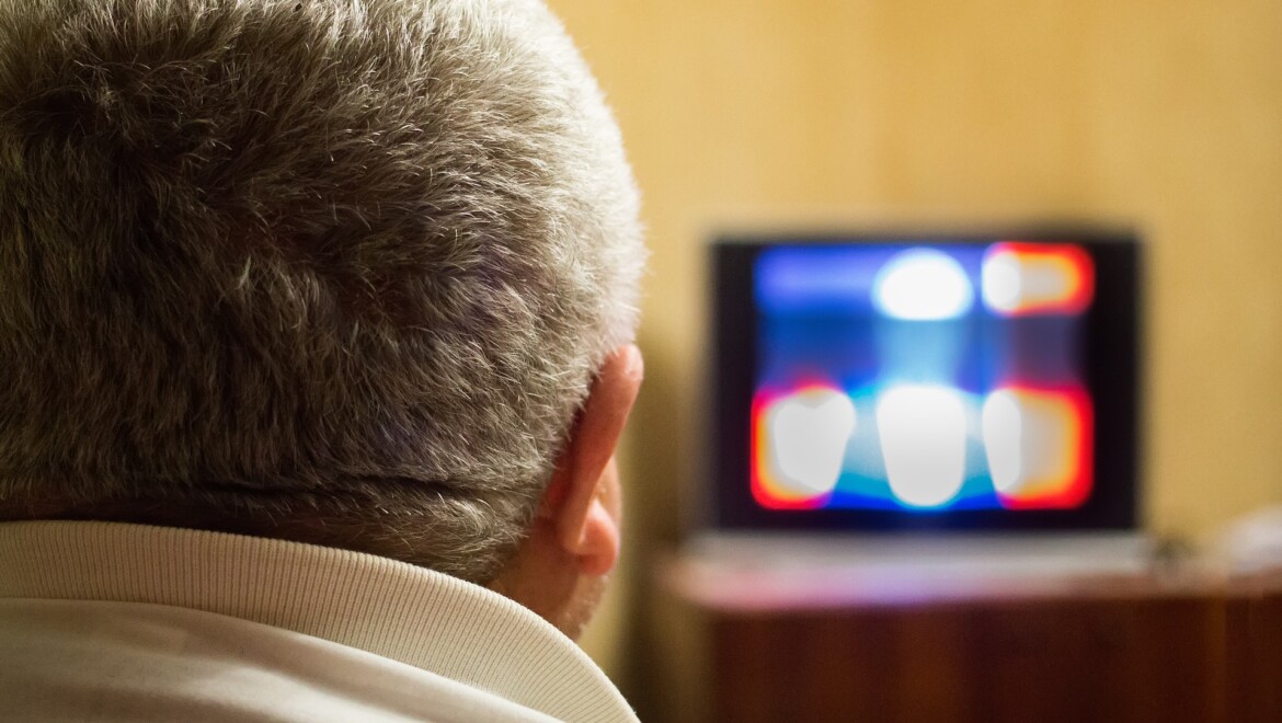 En gråhårig man tittar på tv.