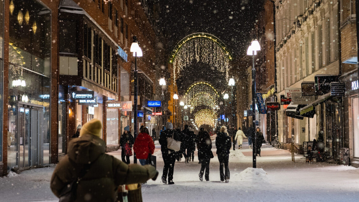 Snöig shoppinggata upplyst med julbelysning med personer som strosar runt.