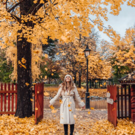 Adaras i vit kappa och vit mössa som kastar gula höstlöv ovanför sig.