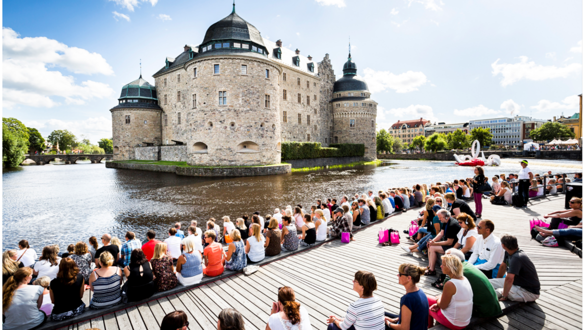 Många människor sitter på soldäcket framför Örebro slott.