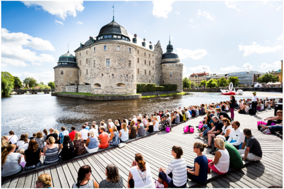 Många människor sitter på soldäcket framför Örebro slott.