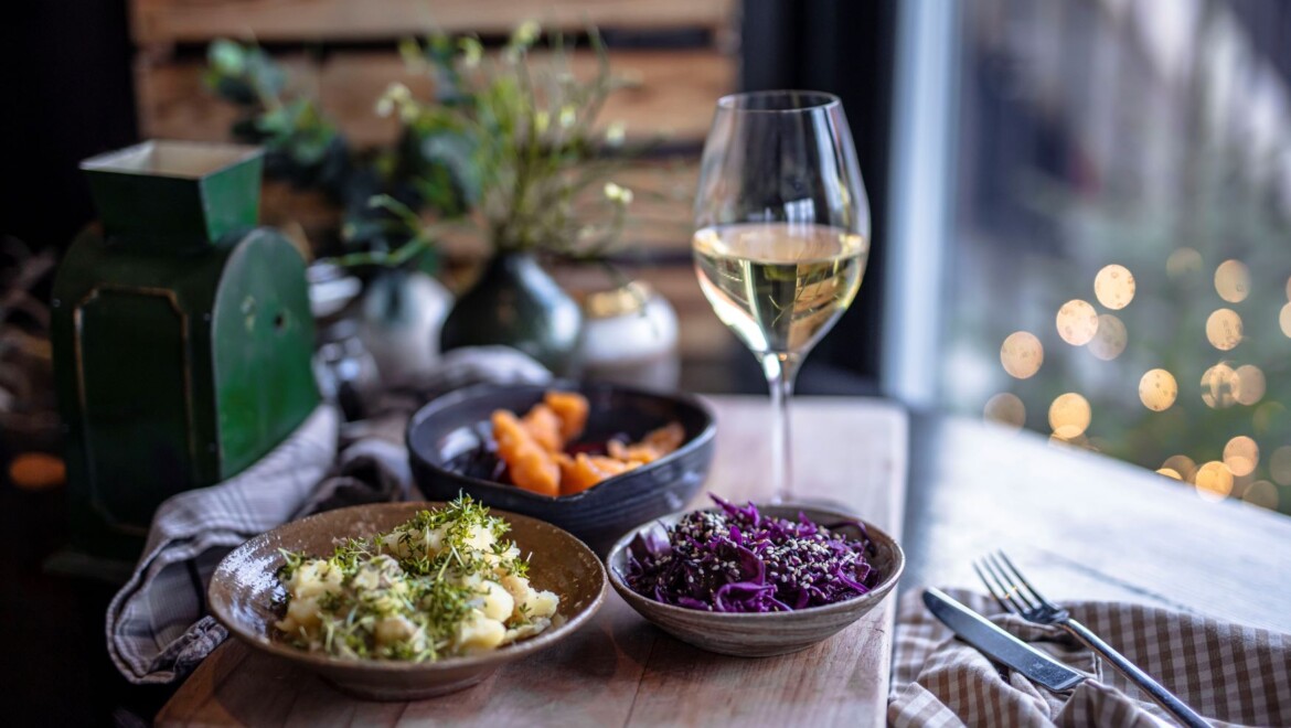 Tre tallrikar med färgglada grönsaker på. Ett glas vitt vin står bredvid.
