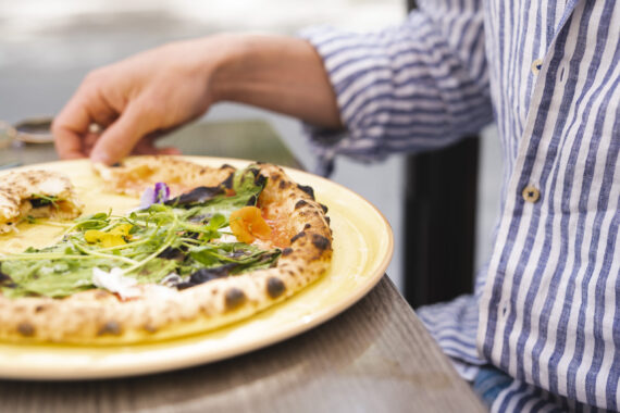 En pizza med gröna blad som topping. En randig skjorta syns i bakgrunden.