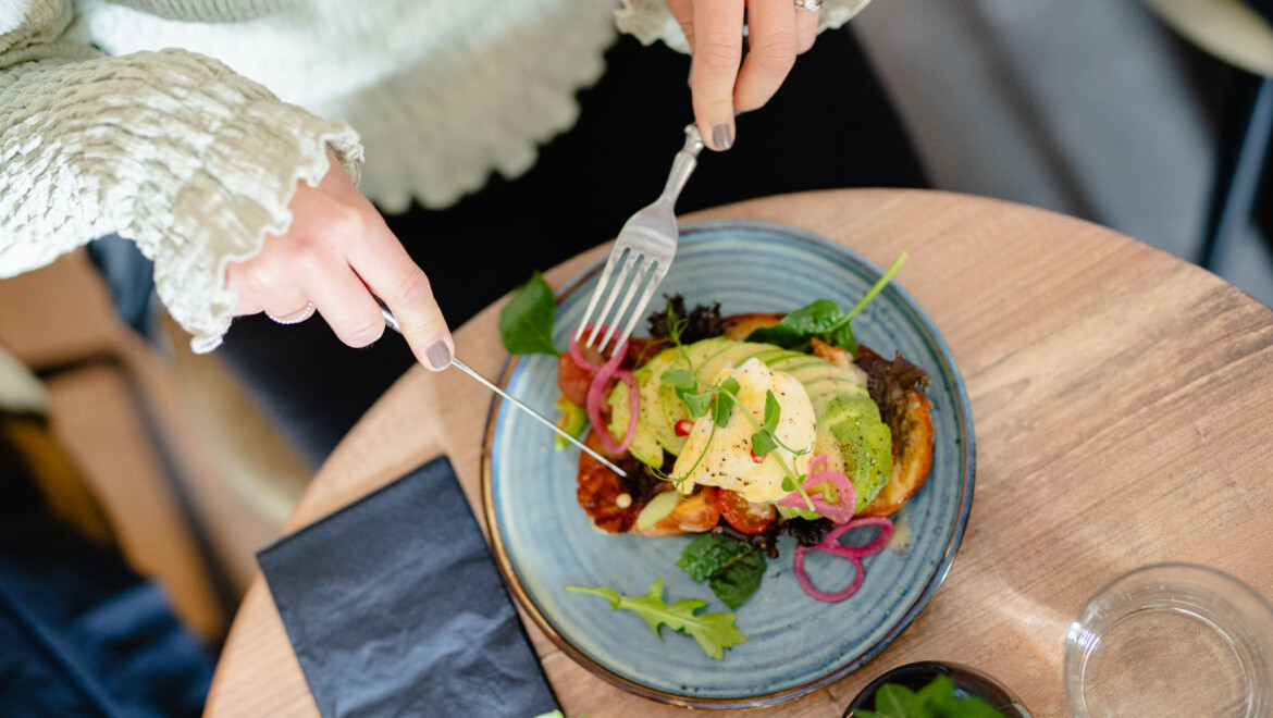 En tjej i plisserad tröja äter brunch, en smörgås med ägg och avokado.