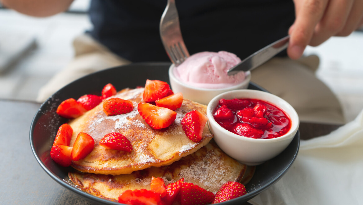 En tallrik med pannkakor, jordgubbar och jordgubbsglass.