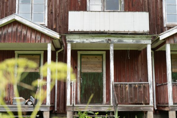 Ett fallfärdigt hus med gråröd fasadfärg.