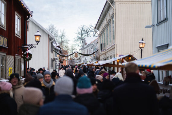 Ett myller av folk som går vinterklädda bland marknadsstånd mellan gamla trähus.
