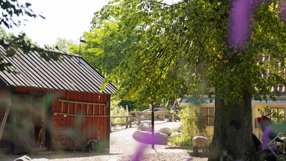 Ett rött trähus i en lekpark. Bakom ett träd skymtar även ett gult hus.