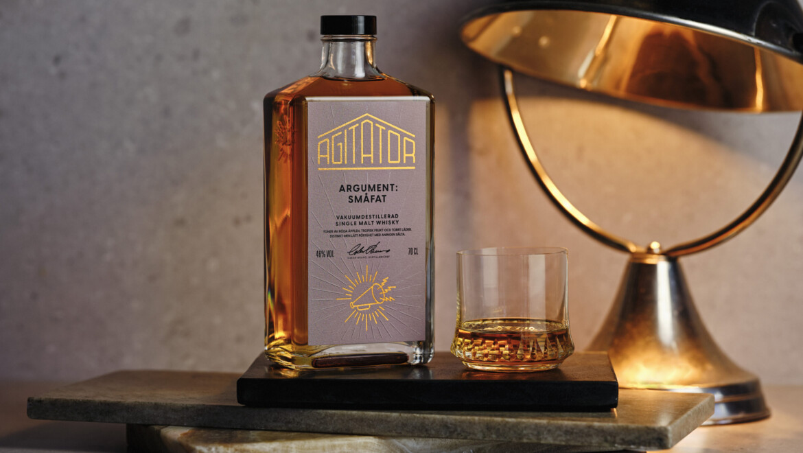 En whiskyflaska står bredvid ett glas med whisky och en antik lampa.