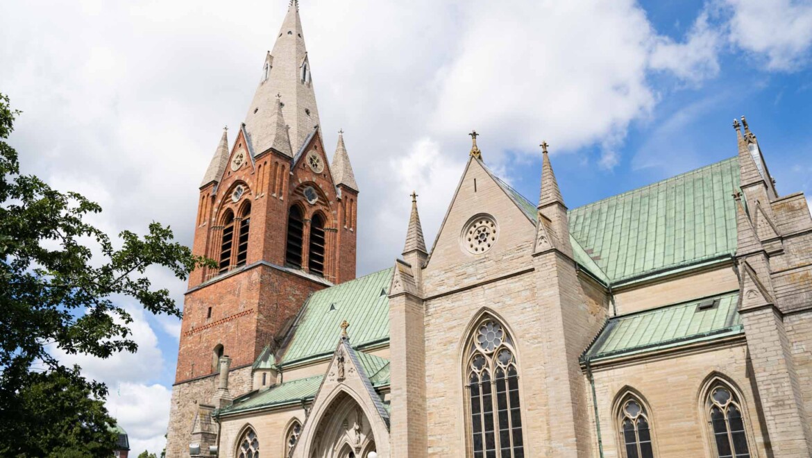 En kyrka i tegel och grå sten med spetsigt kyrktorn.