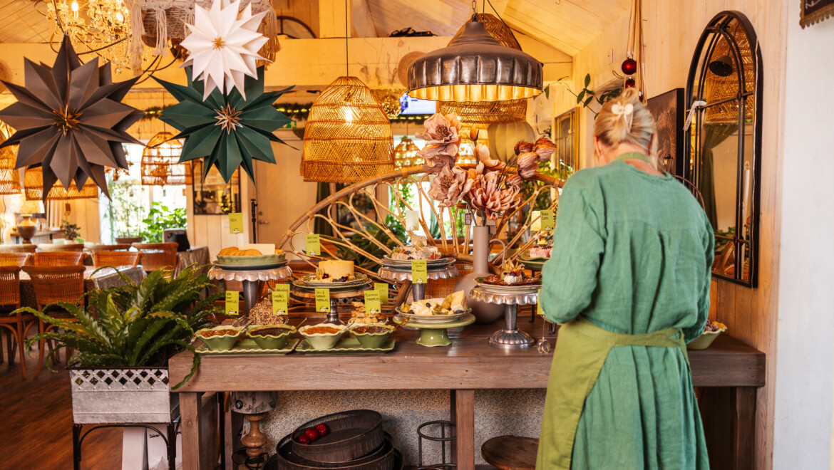 En kvinna i gröna kläder står med ryggen till, vid ett bord med lyxfrukost framdukat.