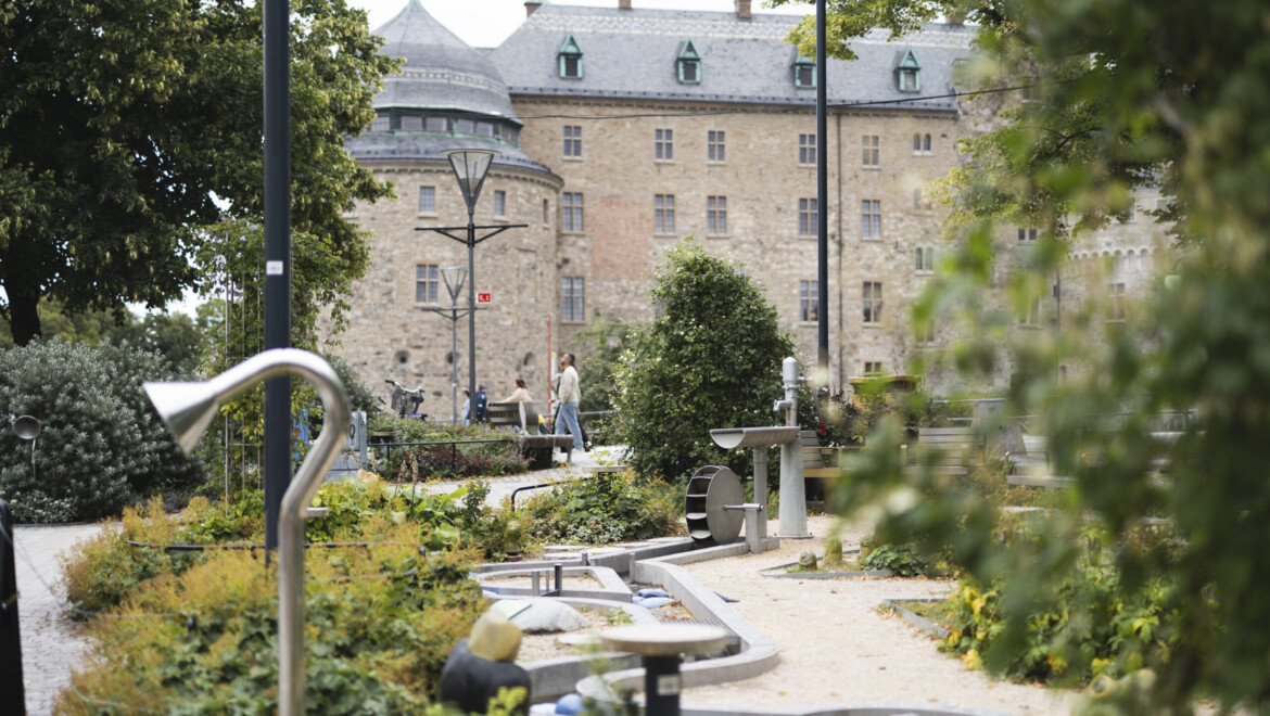 Grönskande lekmiljö syns med stort stenslott i bakgrunden.