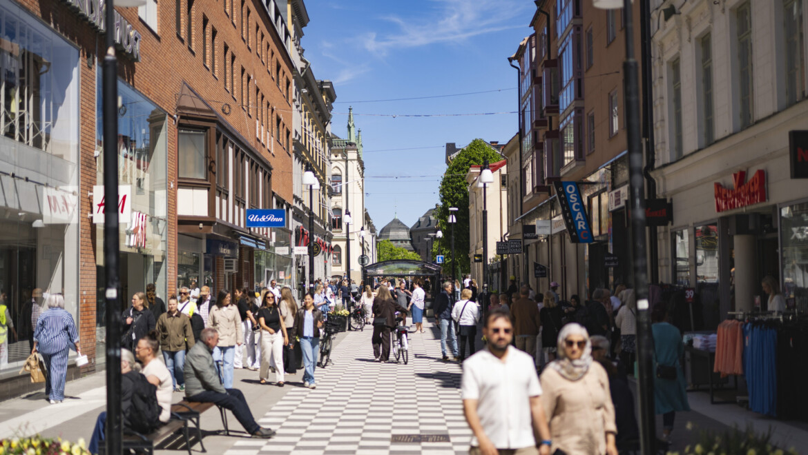En shoppinggata är full med människor. Det är soligt väder.