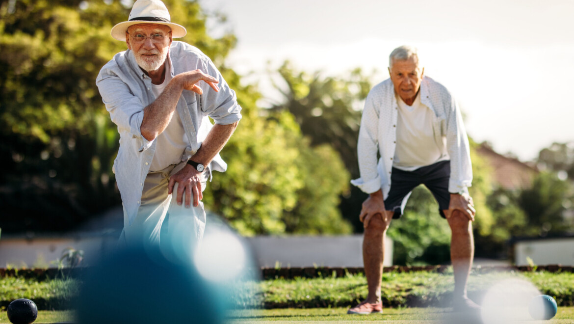 An older man throwing a boules ball while another older man watches